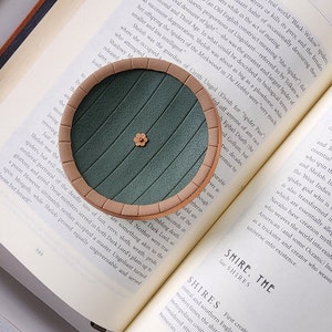 Pu&ograve; includere: Un tappetino rotondo verde e marrone con un motivo floreale. Il tappetino &egrave; fatto per assomigliare all'ingresso di una tana di hobbit.