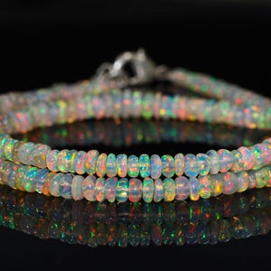 Puede incluir: Un collar de cuentas de ópalo iridiscente, con un arcoíris de colores, enhebrado en una cadena de plata. Las cuentas son pequeñas y redondas, y la cadena es delicada.