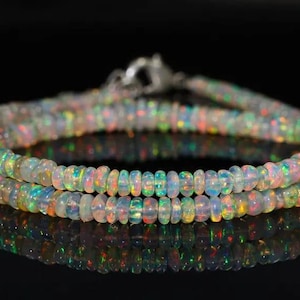 May include: A strand of small, circular, translucent opal beads featuring a play of color with flashes of green, orange, and pink. The beads are strung together in a continuous loop, finished with a silver-toned metal clasp at the back.