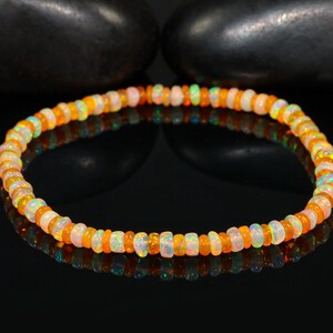 May include: A bracelet made of small, round opal beads. The beads display a mix of colours, including orange, white, and green. The gemstones are strung together, forming a circular bracelet. The bracelet is approximately 18 cm in circumference.