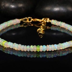 May include: A delicate bracelet made with white opal beads and a few green opal beads. The bracelet is made with a gold clasp.