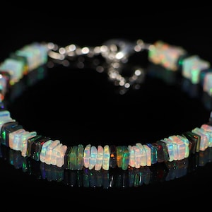 Puede incluir: Un brazalete de cadena de plata con cuentas de ópalo de forma cuadrada. Las cuentas son una mezcla de blanco, negro y verde.