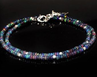 May include: A double-strand bracelet with small, iridescent opal beads in blue, green, and red hues. It has a silver clasp. The beads are about 0.2 cm in diameter. The bracelet is a piece of jewellery.