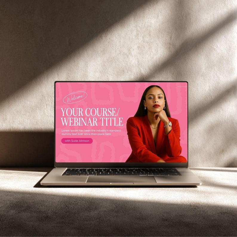 May include: A silver laptop displays a webinar title on its screen. The screen features a pink background with the text "YOUR COURSE/ WEBINAR TITLE" and a woman in a red blazer. The laptop is on a neutral-toned surface.