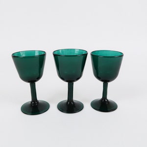 May include: Three dark green glass wine glasses with a rounded bowl and a stem.