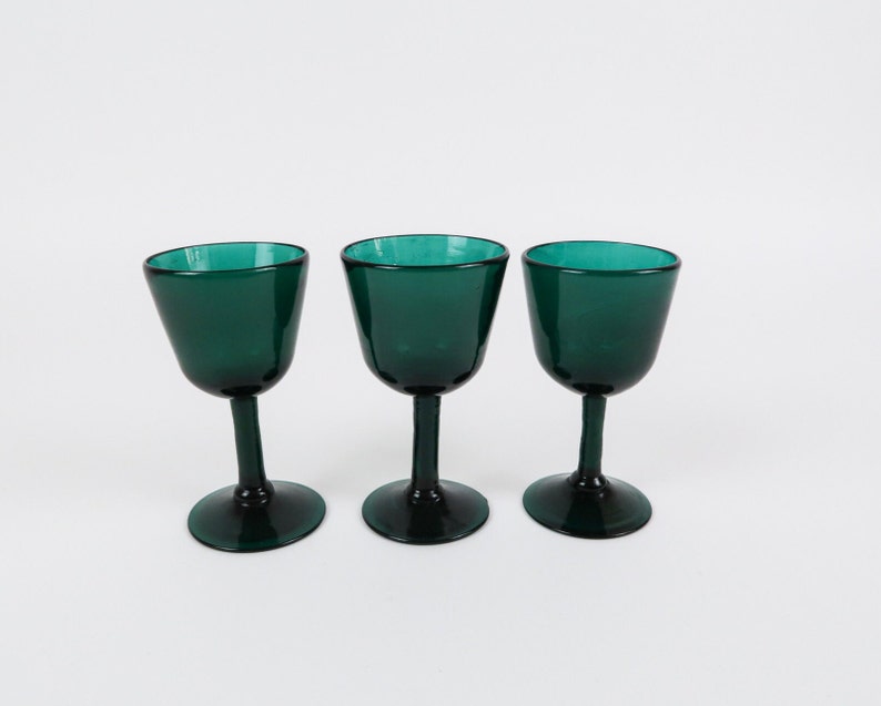May include: Three dark green glass wine glasses with a rounded bowl and a stem.