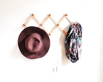 May include: A brown felt hat and a colorful patterned scarf hanging on a wooden rack with a silver chain necklace.