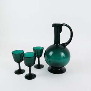 May include: A set of four teal green glass drinking glasses, including a pitcher with a rounded body and a handle.