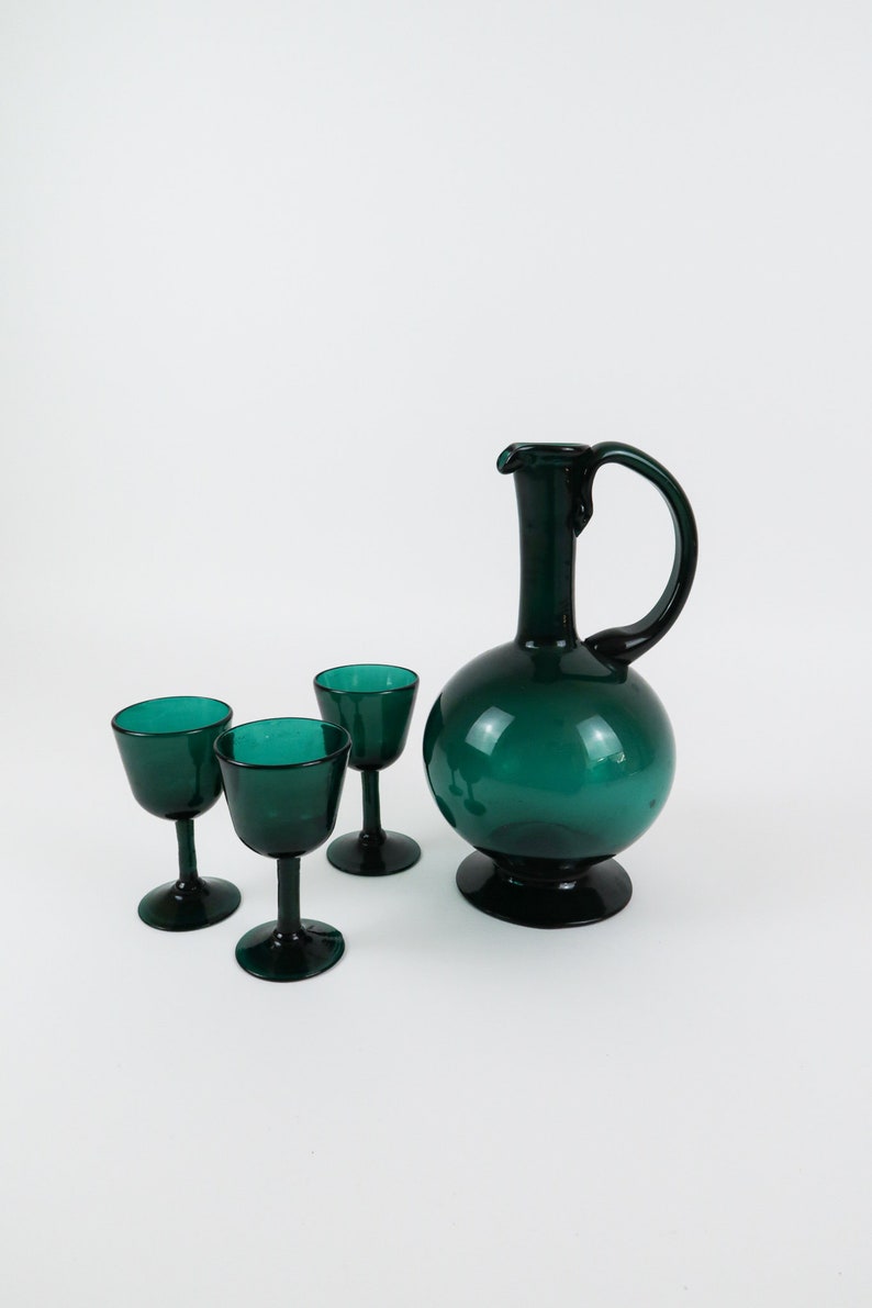 May include: A set of four teal green glass drinking glasses, including a pitcher with a rounded body and a handle.