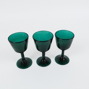 May include: Three dark green glass wine goblets with a round bowl and a stem.