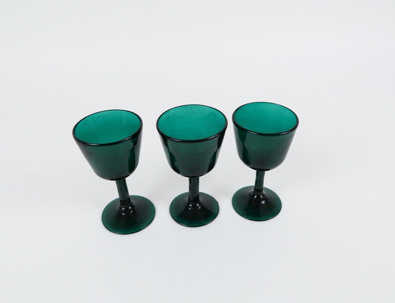 May include: Three dark green glass wine goblets with a round bowl and a stem.