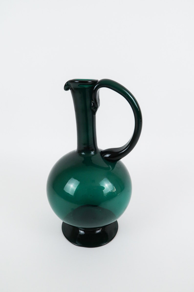 May include: A dark green glass pitcher with a round body and a curved handle.