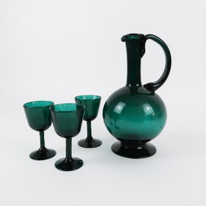 May include: A set of three teal green glass shot glasses and a matching teal green glass decanter with a round body and a curved handle.