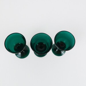 May include: Three teal green stemmed glasses with a rounded bowl shape.