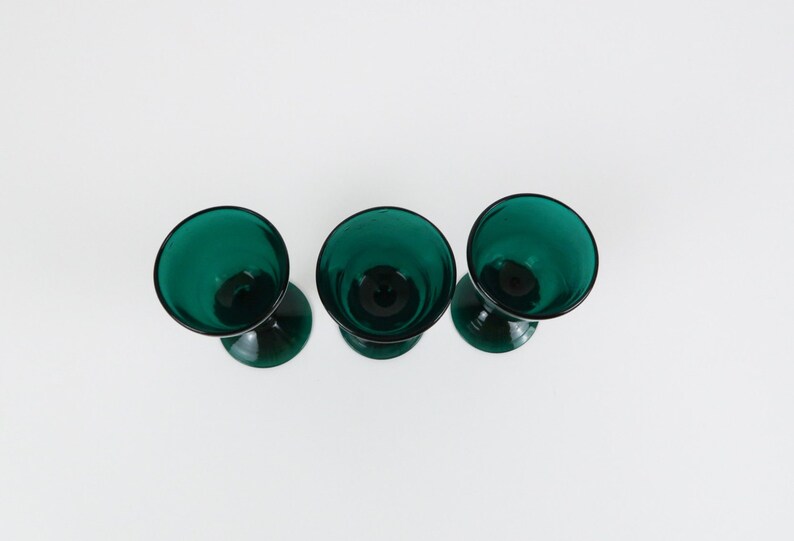 May include: Three teal green stemmed glasses with a rounded bowl shape.