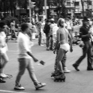 May include: A monochrome image of a person rollerblading through a crowd. The person is wearing a helmet and underwear. Other people are walking in the background.