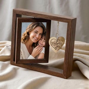 May include: A wooden photo frame with a picture of a woman and a child. A heart-shaped charm with "Mother's Day" engraved hangs from the frame. The frame is a dark brown color and sits on a cream-colored surface.