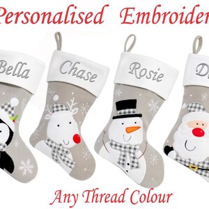 May include: Four personalised embroidered Christmas stockings. Each stocking features a different festive character: a penguin, reindeer, snowman, and Santa Claus. The names Bella, Chase, Rosie, and Demi are embroidered on the white cuff.