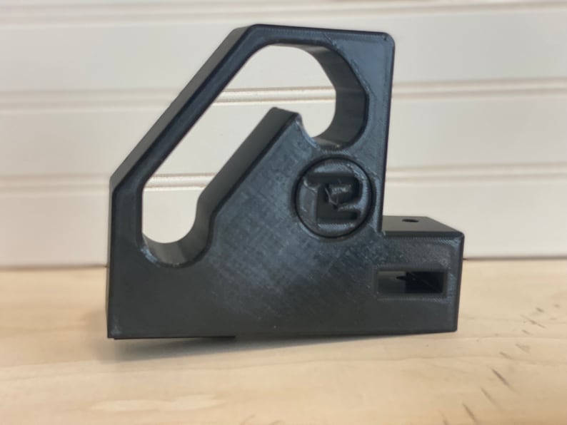 May include: Black plastic 3D printed corner bracket with a hole in the center and a small rectangular slot on the side. The bracket has a logo that says "T2" on it.