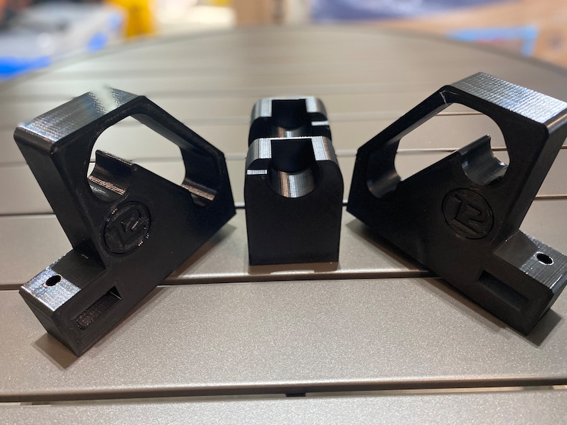 May include: Three black plastic 3D printed corner brackets with a circular hole in the center of each bracket. The brackets have a logo on the side.