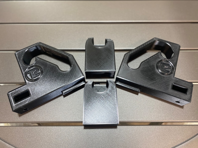 May include: Four black plastic 3D printed wall mounts with a hook and a small hole on the side. The mounts have a circular logo with the letter "Z" inside.