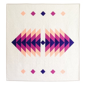 May include: A white quilt with a geometric pattern in shades of pink, peach, and purple. The pattern is symmetrical and resembles a stylized eye.