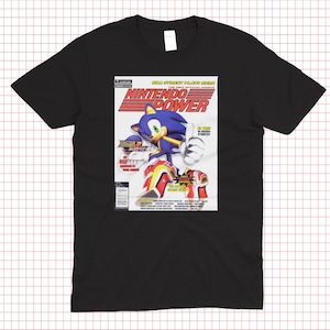 May include: Black t-shirt featuring a graphic of Sonic the Hedgehog on a mock Nintendo Power magazine cover. The magazine cover has the title "Nintendo Power" in red and white, with the Sonic the Hedgehog character in the center.