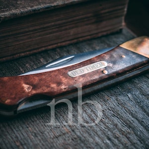 Pode incluir: Um canivete de bolso com cabo marrom, lâmina prateada e as palavras "Old Timer" gravadas no cabo.