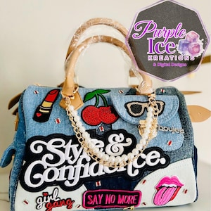 May include: Denim handbag with a light brown handle and a gold chain. The bag is decorated with patches including a lipstick, cherry, sunglasses, and the words "Style & Confidence" and "girl gang".