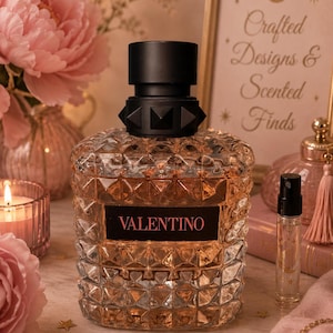 May include: A glass perfume bottle with a textured, diamond-patterned surface and a black label featuring the word VALENTINO in pink lettering. The bottle has a black cap with a studded collar and contains a light peach-colored liquid fragrance.