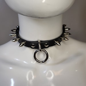 Collar delgado de cuero negro, pequeñas púas de latón y correa central.
