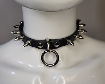 Collar delgado de cuero negro, pequeñas púas de latón y una correa central.