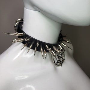 May include: Black leather choker necklace with silver-colored spikes and a pentagram charm. The choker is displayed on a white mannequin, showcasing its punk rock or gothic style. The spikes are evenly spaced around the collar.