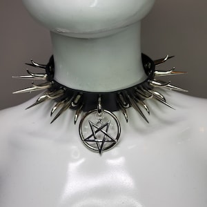 May include: Black leather choker necklace with silver-colored spikes and a pentagram pendant. The choker is displayed on a white mannequin, showcasing the gothic and alternative style of the jewelry.