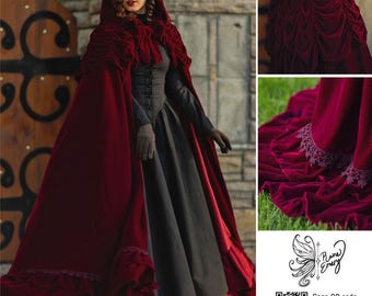 Puede incluir: Una capa con capucha de terciopelo rojo intenso con un dobladillo con volantes y ribete de encaje, capucha fruncida y cierre de lazo frontal. La capa se lleva sobre un vestido negro de manga larga. Incluye el logotipo de Prairie Emery y un código QR.