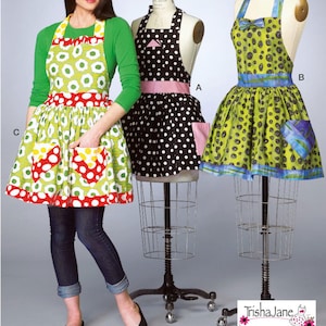 Könnte beinhalten: Ein Schnittmuster für drei verschiedene Stile von Schürzen. Die Schürzen werden auf Schaufensterpuppen und einer Person gezeigt. Die Schürzen sind aus verschiedenen Stoffen mit verschiedenen Mustern gefertigt, darunter Punkte, Blumen und geometrische Formen. Die Schürzen sind alle in leuchtenden Farben, darunter Grün, Schwarz, Rot und Blau.