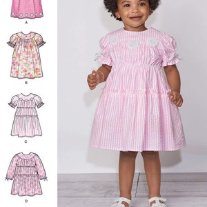 May include: A sewing pattern for a baby girl's dress. The pattern includes four different styles: a solid pink dress with a lace trim, a floral print dress, a striped dress, and a tiered dress. The pattern is for sizes 12 months to 4T.