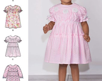 May include: A sewing pattern for a child's dress featuring four variations labeled A, B, C, and D. The designs include options with short or long sleeves, floral or striped fabrics, and decorative lace or flower accents on the bodice and collar.