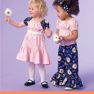 May include: Sewing pattern for two girls' dresses. One dress is pink with a white waistband and a ruffled hem. The other dress is a blue and white floral print with a ruffled hem.