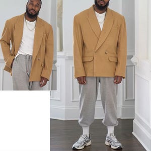 Op de afbeelding: Een beige dubbelrijig blazer met een ontspannen pasvorm. De blazer heeft een reverskraag en twee klepzakken. Het model draagt de blazer met een wit T-shirt en grijze joggingbroek.