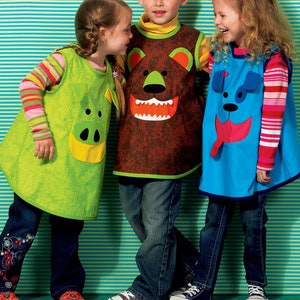May include: Three children wearing colorful aprons with animal faces. The aprons are green, brown, and blue. The children are wearing jeans and casual shoes.