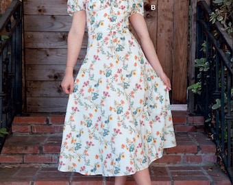 Könnte beinhalten: Ein weißes Midikleid mit Blumenmuster. Das Kleid hat einen quadratischen Ausschnitt, kurze Puffärmel und ein tailliertes Oberteil. Der Rock ist weit und fließt bis zum Knie. Das Kleid wird von einem Model gezeigt, das auf einer Backstein-Treppe steht.