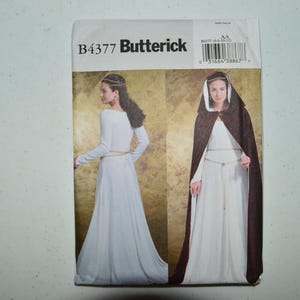 May include: A Butterick B4377 sewing pattern envelope featuring two illustrations of a long white dress with long sleeves and a thin belt, one showing a dark brown hooded cloak worn over the dress. The text B4377 Butterick is printed at the top.