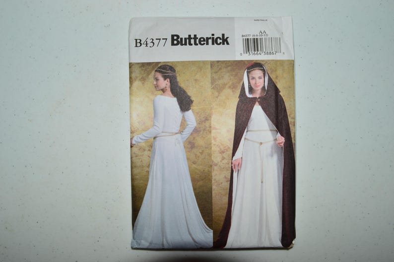 May include: A Butterick B4377 sewing pattern envelope featuring two illustrations of a long white dress with long sleeves and a thin belt, one showing a dark brown hooded cloak worn over the dress. The text B4377 Butterick is printed at the top.
