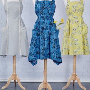 Puede incluir: Tres patrones de costura de delantal diferentes que se muestran en maniquíes. Los delantales son de varios colores y patrones, incluyendo azul con búhos, amarillo con flores y gris con encaje blanco.
