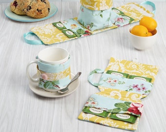 May include: Sewing pattern for a tea cozy and tea bag holder. The cozy is made of blue and yellow fabric with floral patterns. The tea bag holder is made of yellow fabric with a floral pattern and has a handle. The pattern includes instructions for making both items.