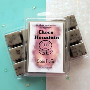 May include: A clear plastic container holding scented wax melts. The label reads "Choco Mountain Coco Puffs" with a flower graphic. The wax melts are a light brown color with darker speckles. The net weight is 2.5oz (70g).