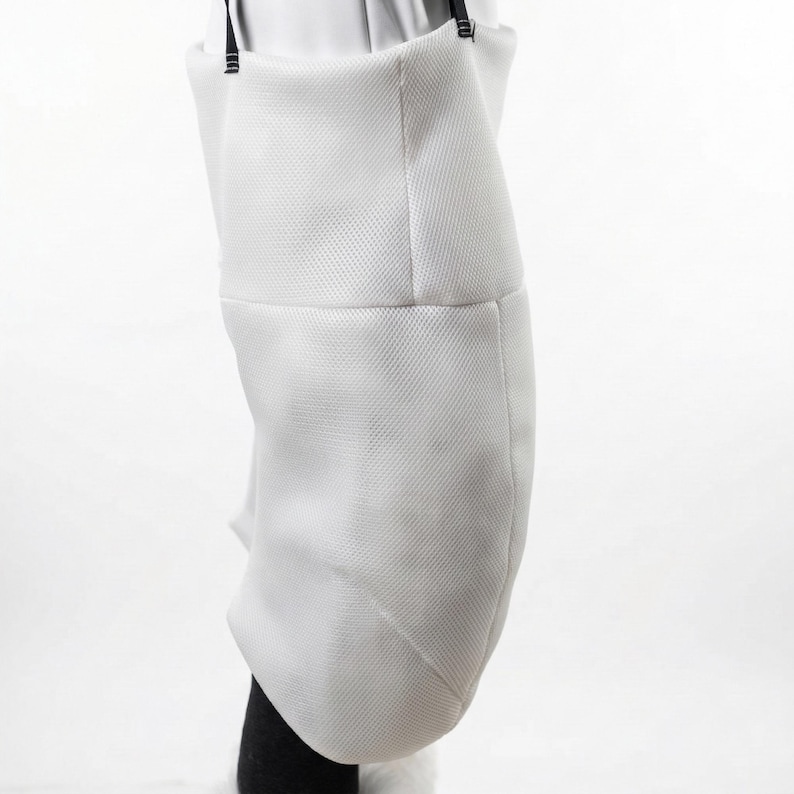 May include: A white fencing jacket, made of a textured fabric, is shown from the waist down. The jacket has a structured shape with a slight curve and is held up by black straps. The lower portion of a black garment is visible.