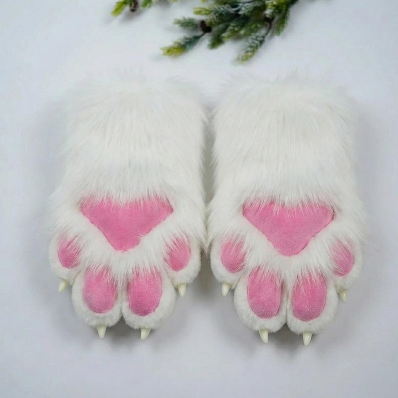 A pair of white furry paw-shaped gloves with pink paw pads, placed on a white surface.