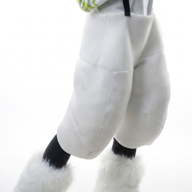 May include: White padded pants with a textured surface, black suspenders, and fluffy white leg warmers. The pants have a unique, rounded design. The outfit is likely part of a costume or performance wear.